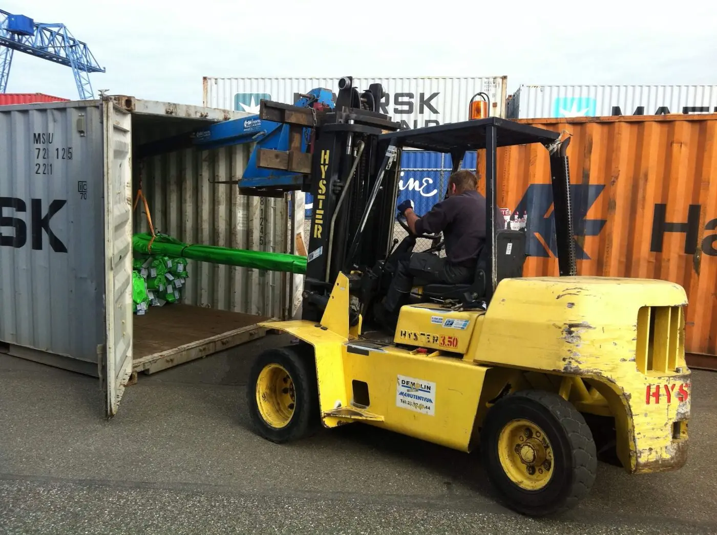 Forklift stripping green-wrapped pipes from a container at the terminal